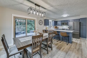 A modern kitchen with dark cabinets, a central island, and a dining area with wooden chairs and a table. - Fishing & Creek On-site! Red Lodge Family Retreat (Red Lodge)