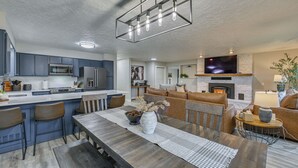 Una cucina moderna con isola centrale, un'area pranzo con tavolo in legno e un soggiorno con camino.