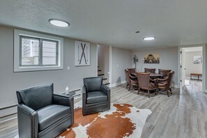 A modern living room with a fireplace, a dining area with a wooden table and chairs, and a large window. - Fishing & Creek On-site! Red Lodge Family Retreat (Red Lodge)