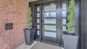 Una porta con cornice nera e pannelli di vetro smerigliato, affiancata da due grandi fioriere nere piene di piante verdi.