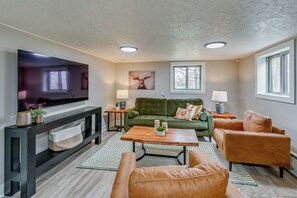 Ein Wohnzimmer mit Flachbildfernseher, grünem Sofa, orangefarbenem Sessel und einem Holztisch.