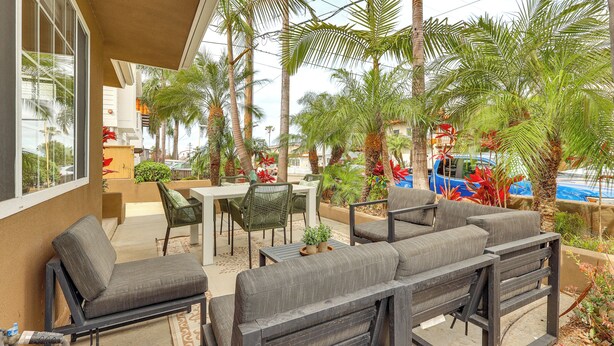 An outdoor patio with a table and chairs, surrounded by palm trees and a view of a swimming pool.