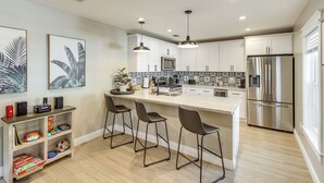 Una cocina moderna con una isla central, taburetes de bar, un refrigerador de acero inoxidable y un microondas.