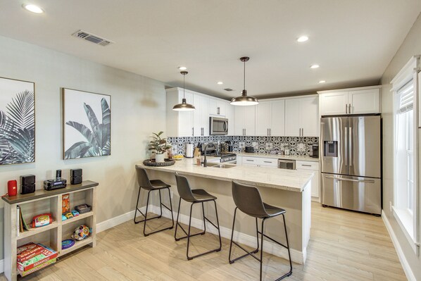 Una cocina moderna con armarios blancos, un refrigerador de acero inoxidable, un microondas y una zona de bar con taburetes.