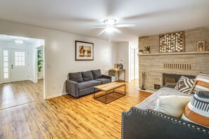 A living room with hardwood flooring, a gray sofa, a coffee table, a fireplace, and a ceiling fan. - Featured on TV! Epic Indoor Pool Sleeps 24 (Bridgman)