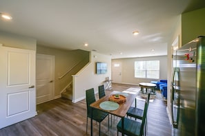 A spacious living area with a wooden dining table, green chairs, a sofa, and a staircase leading to another level.