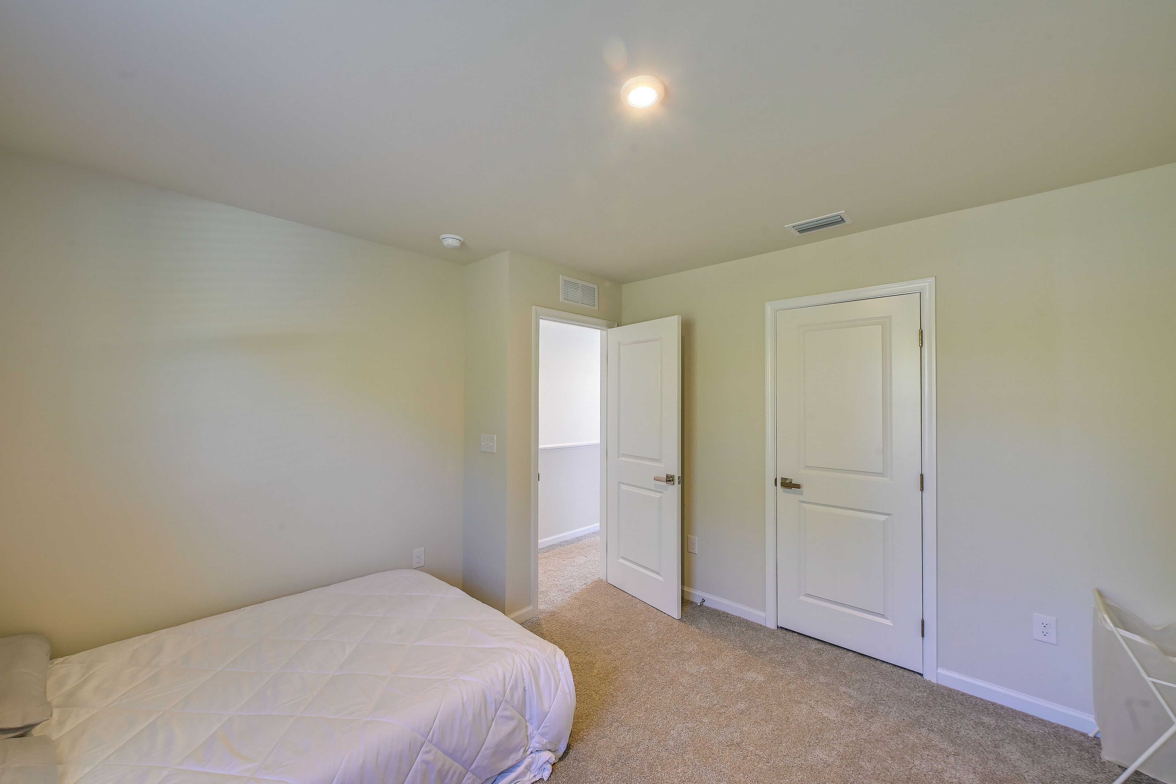 A bedroom with a bed, two doors, and a ceiling light.
