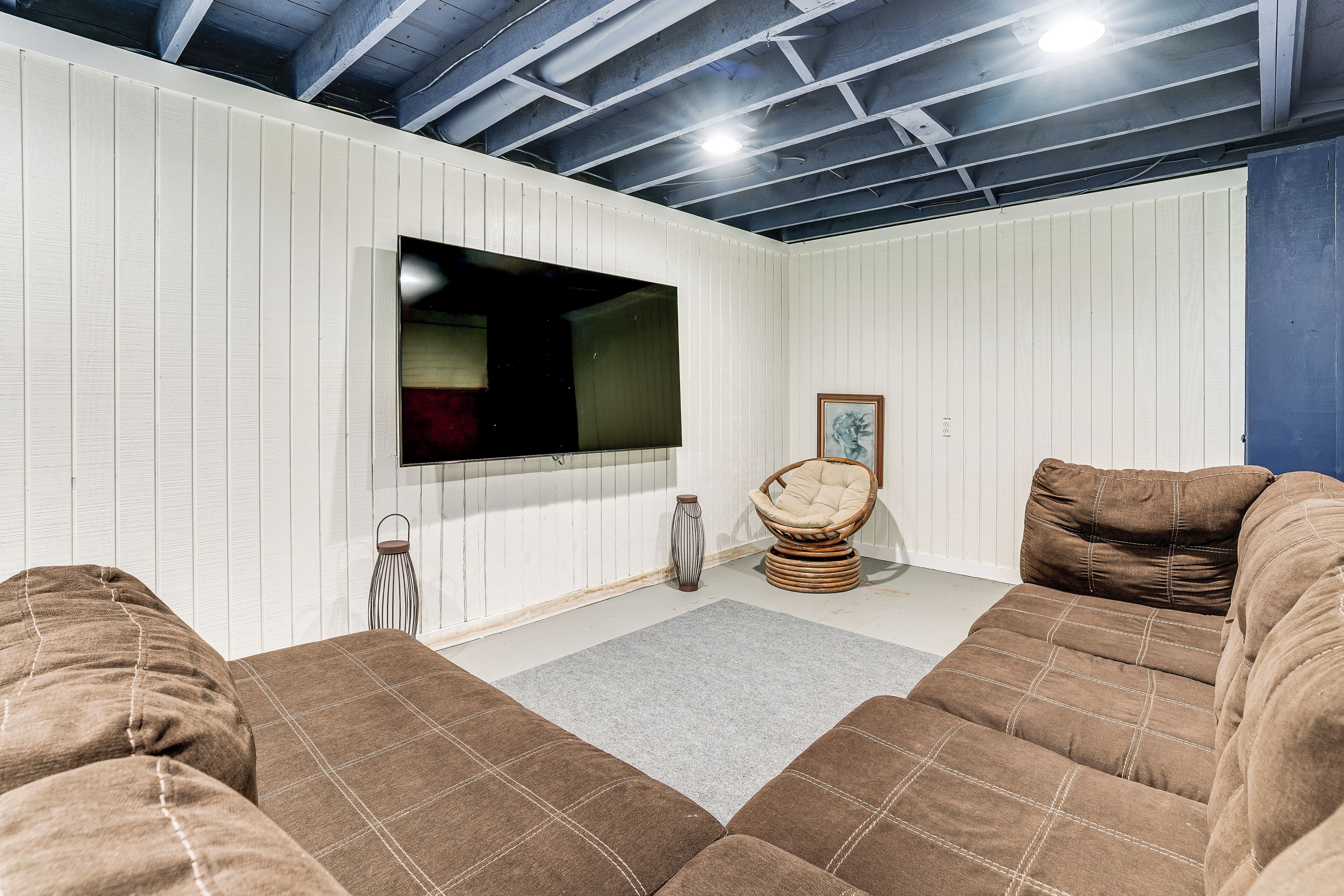 A room with a large flat-screen TV mounted on the wall, a wicker chair, and a brown sofa.