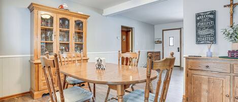A dining room with a wooden table and chairs, a cabinet with glass doors, a ceiling fan, and a wall with a welcome sign.