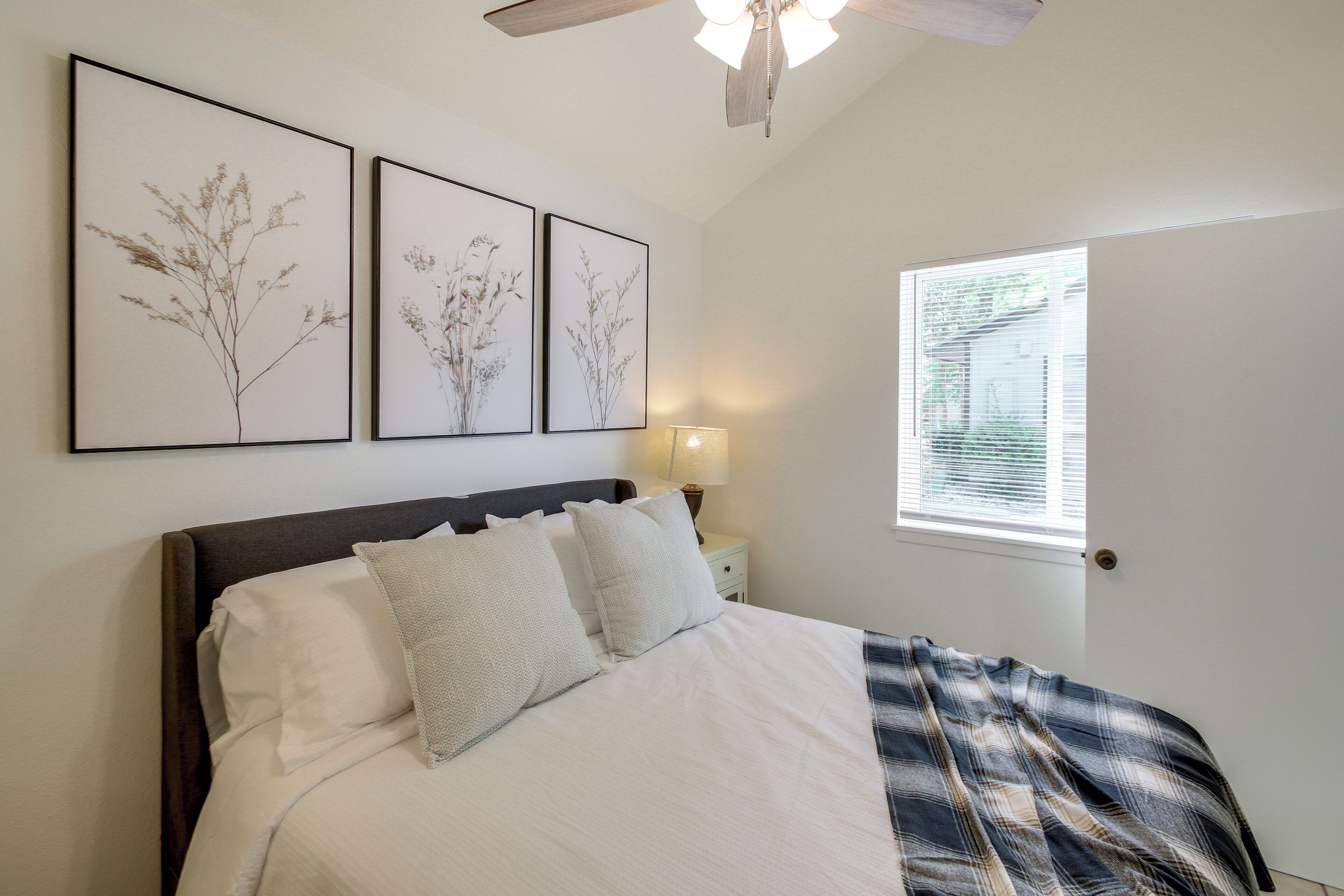 A bedroom with a bed, pillows, a nightstand with a lamp, and wall-mounted artwork.