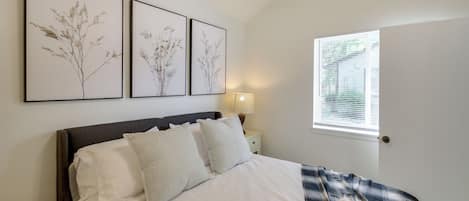 A bedroom with a bed, pillows, a nightstand with a lamp, and wall-mounted artwork.