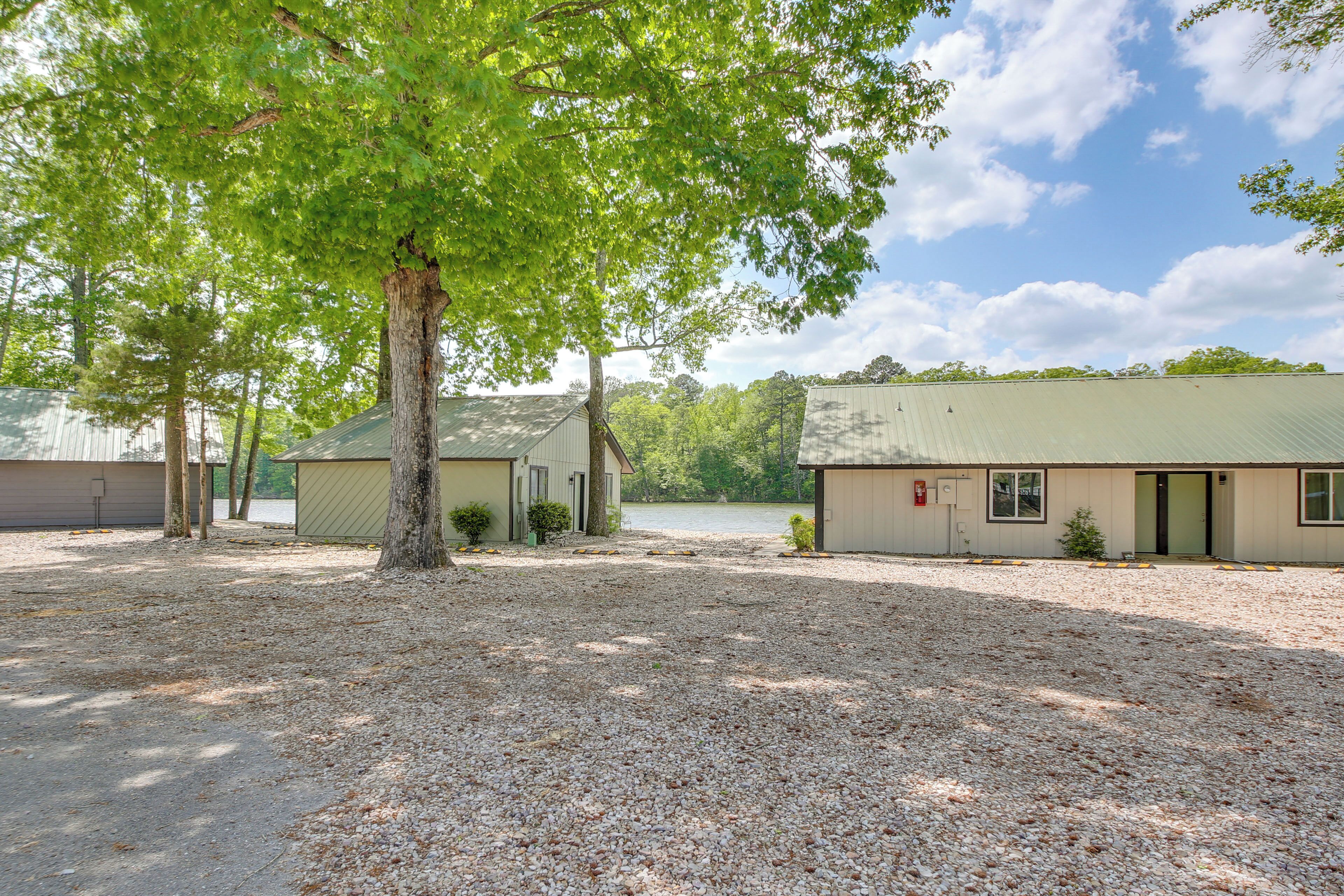 A building with a gravel driveway, a tree in the foreground, and a body of water in the background.