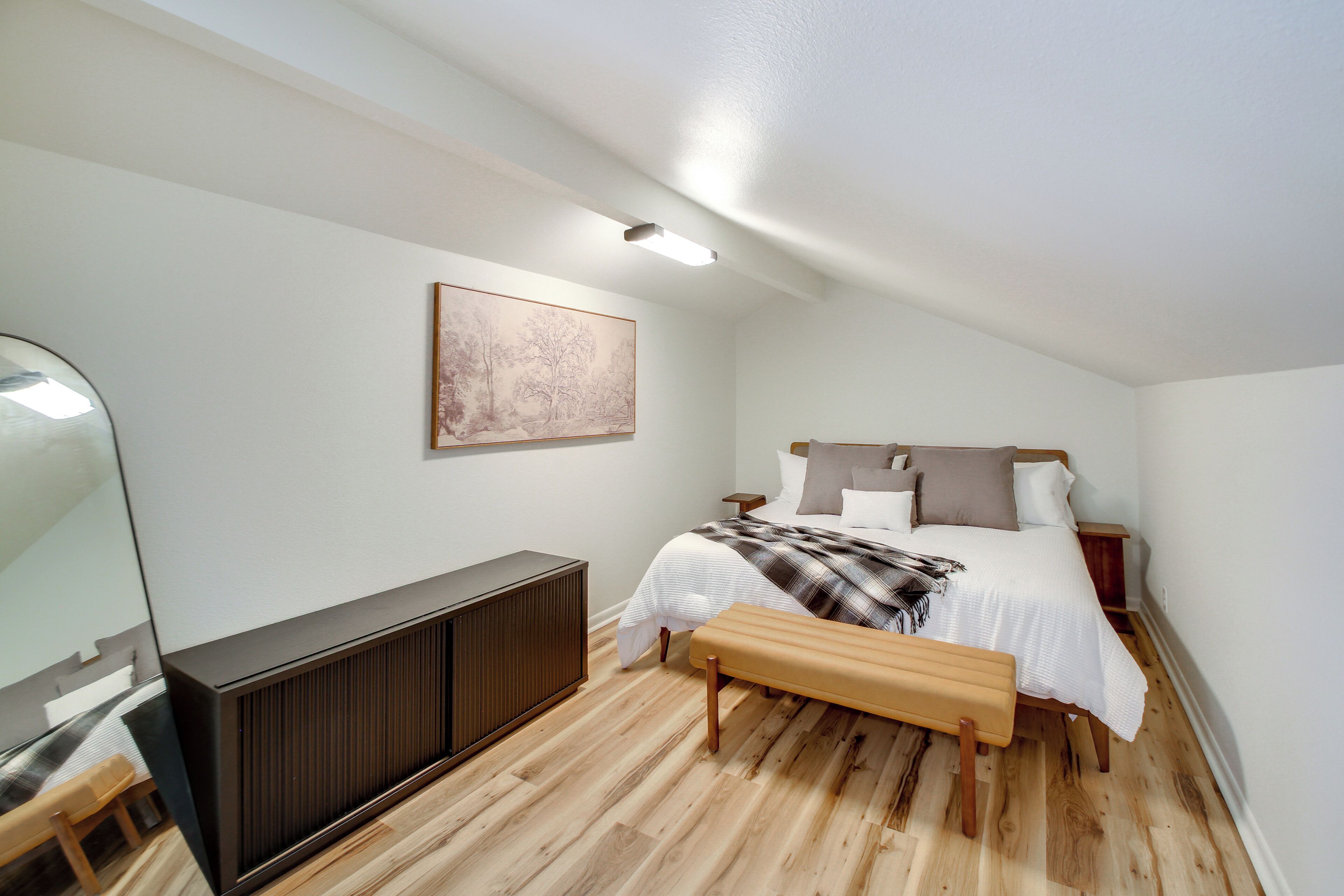 Une chambre à coucher avec un lit, des tables de chevet, un banc, un radiateur et un tableau au mur.