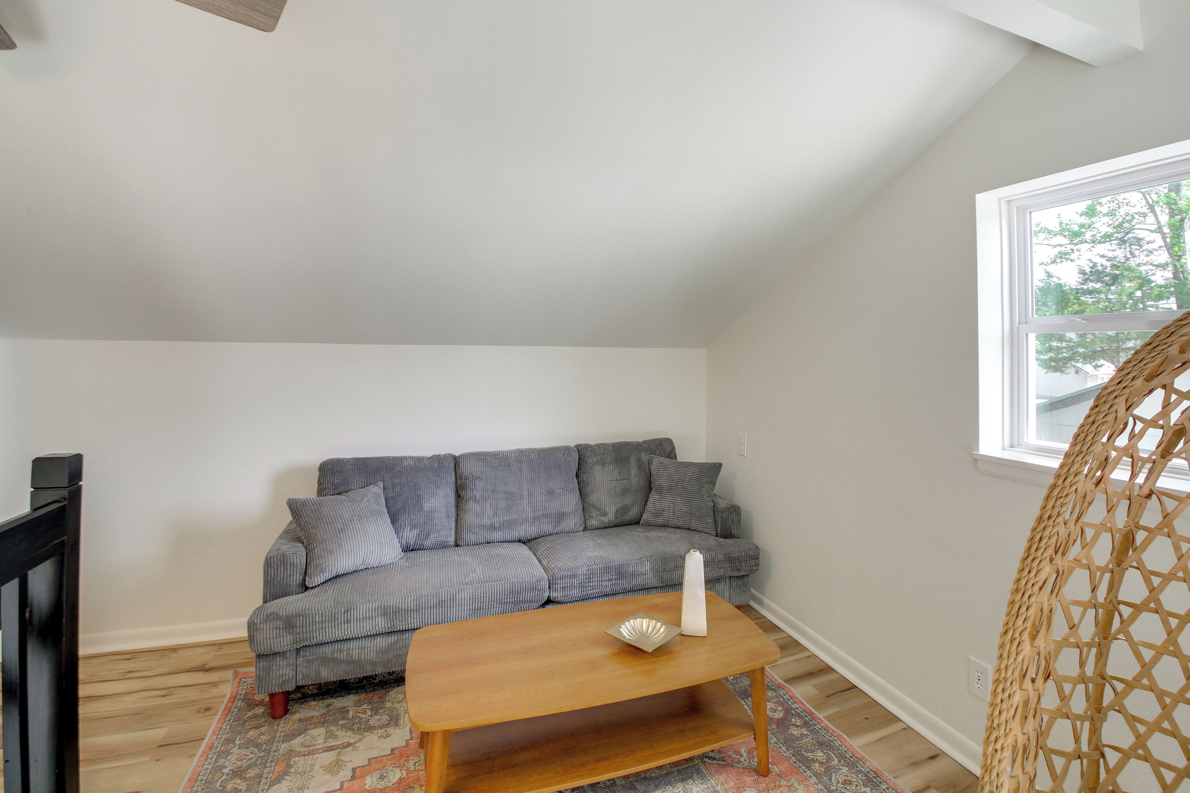 A room with a grey sofa, a wooden coffee table, a wicker chair, and a window.