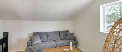 A room with a grey sofa, a wooden coffee table, a wicker chair, and a window.
