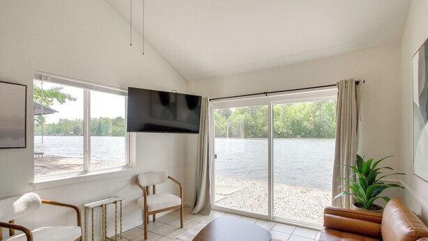 A modern living room with a large window, a flat-screen TV, a sofa, a chair, and a small table. - On-site Boat Launch! Lakefront Hot Springs Cabin (Hot Springs)