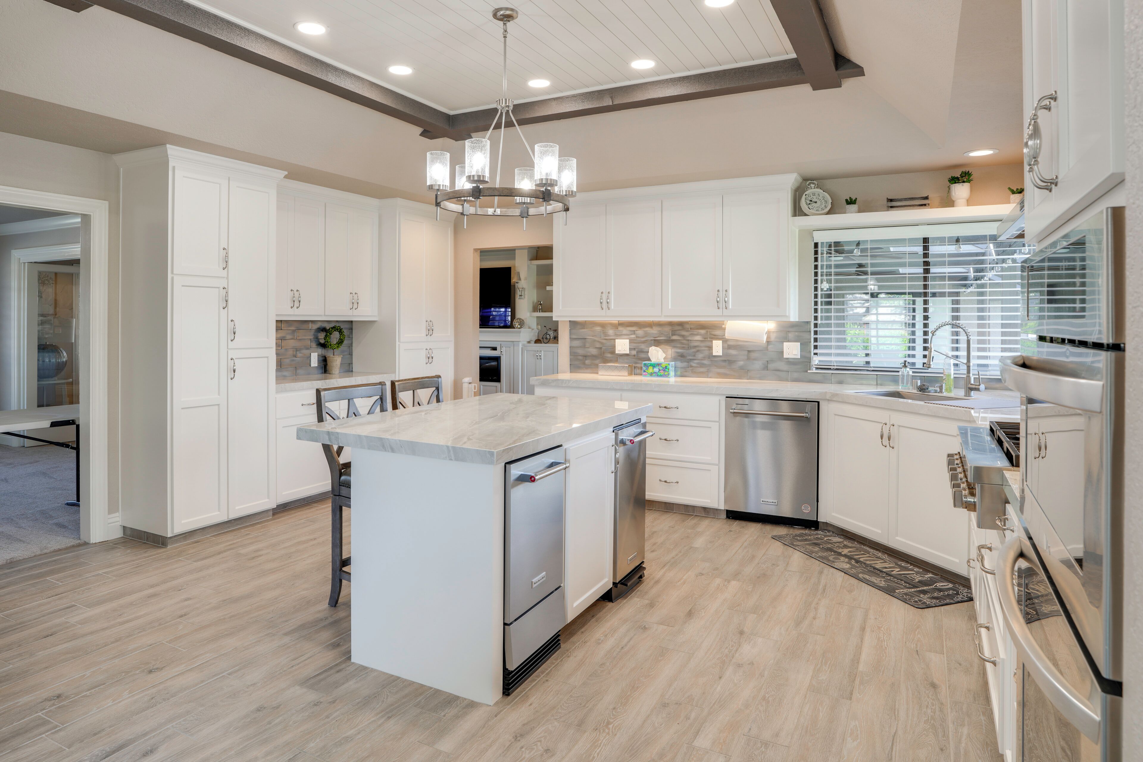 A modern kitchen with white cabinetry, a central island, stainless steel appliances, and a chandelier.