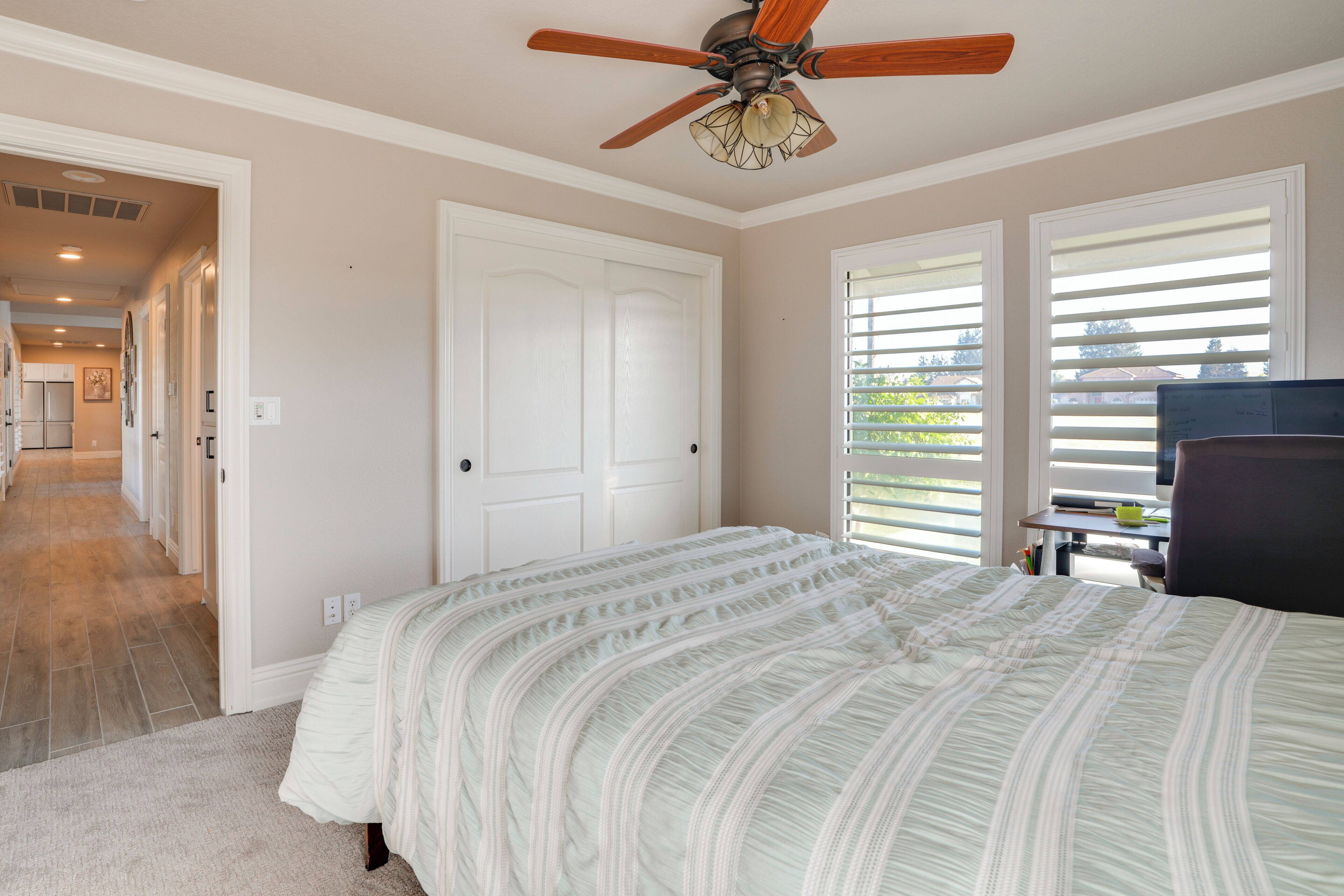 A bedroom with a bed, a ceiling fan, a door, and a window with blinds.