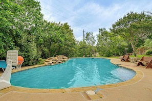 A swimming pool with a stone border, surrounded by trees and a stone wall.