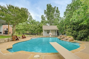 A swimming pool with a stone deck, surrounded by trees and a small building.