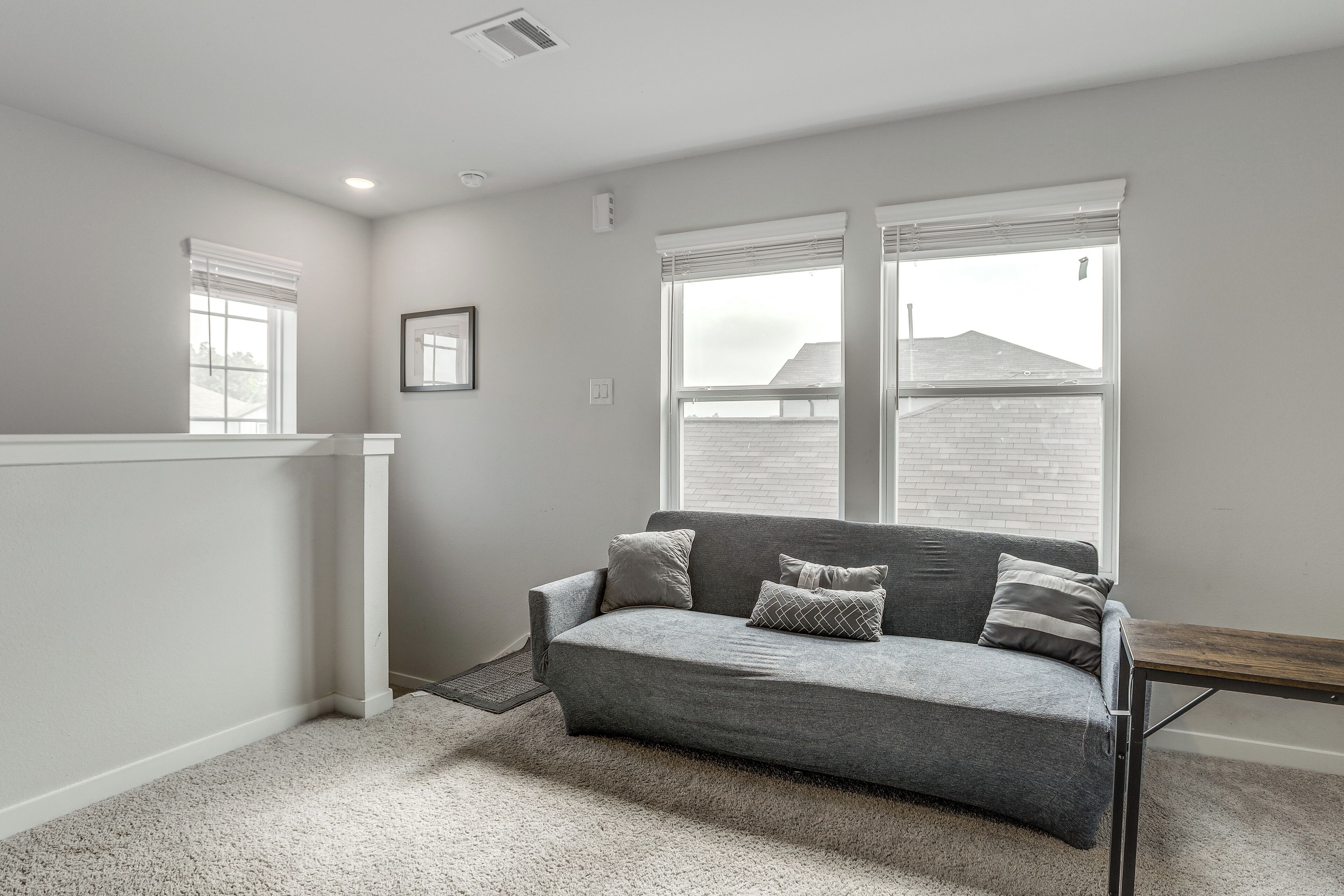 Una habitación con un sofá gris, una mesita y una ventana con persianas.