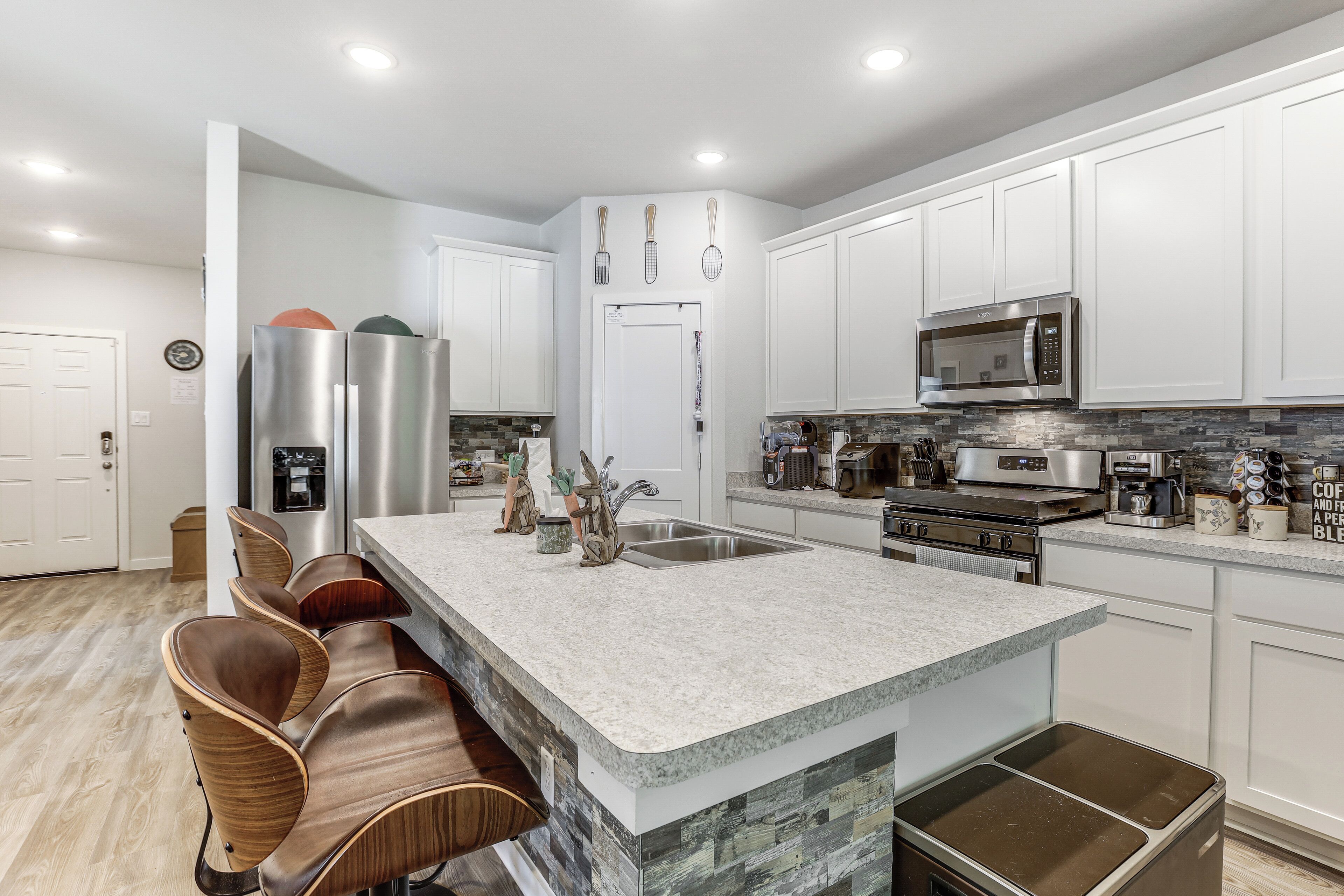 A modern kitchen with white cabinets, stainless steel appliances, a granite countertop, and a built-in island with bar stools.