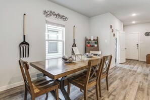A dining area with a wooden table and chairs, a decorative wall piece, and a window with blinds.