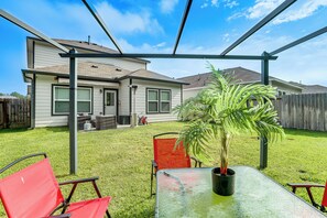 Un espace patio aménagé dans le jardin, avec une table et des chaises, un pot de fleurs et une maison en arrière-plan.