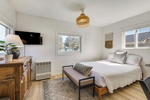 A bedroom with a bed, a bench, a TV, a lamp, a radiator, and a window.