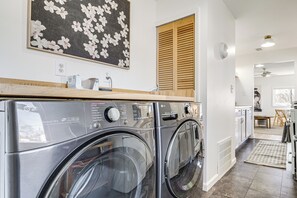 A laundry area with two LG front-loading washers, a wooden countertop, a wall-mounted clock, and a door with wooden shutters. - Walkable 3-unit Escape Near Elk Lake & Bay Access! (Elk Rapids)