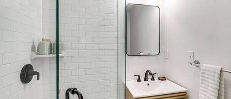 Un baño moderno con cabina de ducha de vidrio, un lavabo blanco y un espejo.