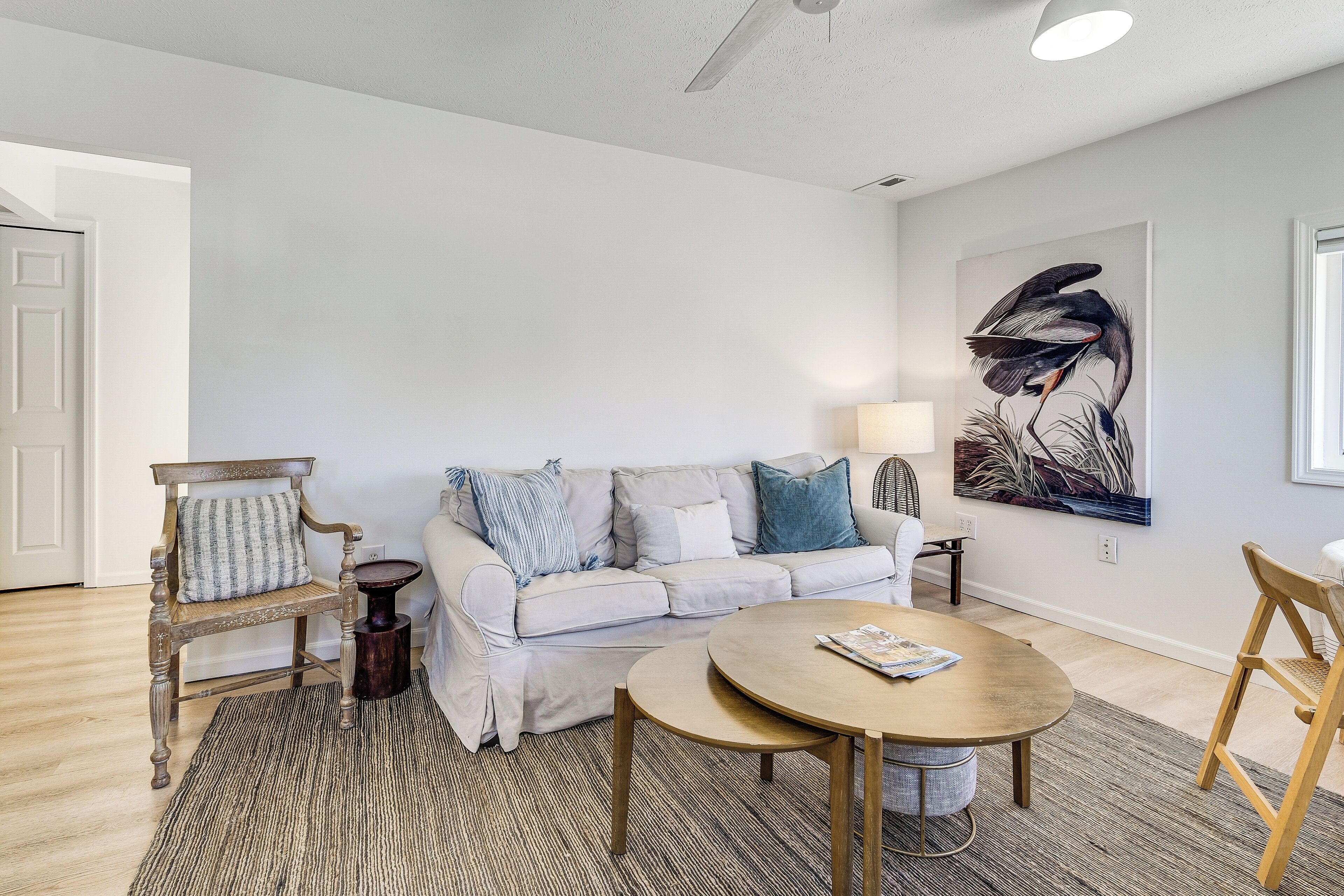A living room with a white sofa, a round wooden table, and a painting on the wall.
