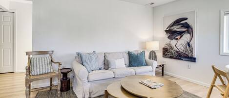 A living room with a white sofa, a round wooden table, and a painting on the wall.