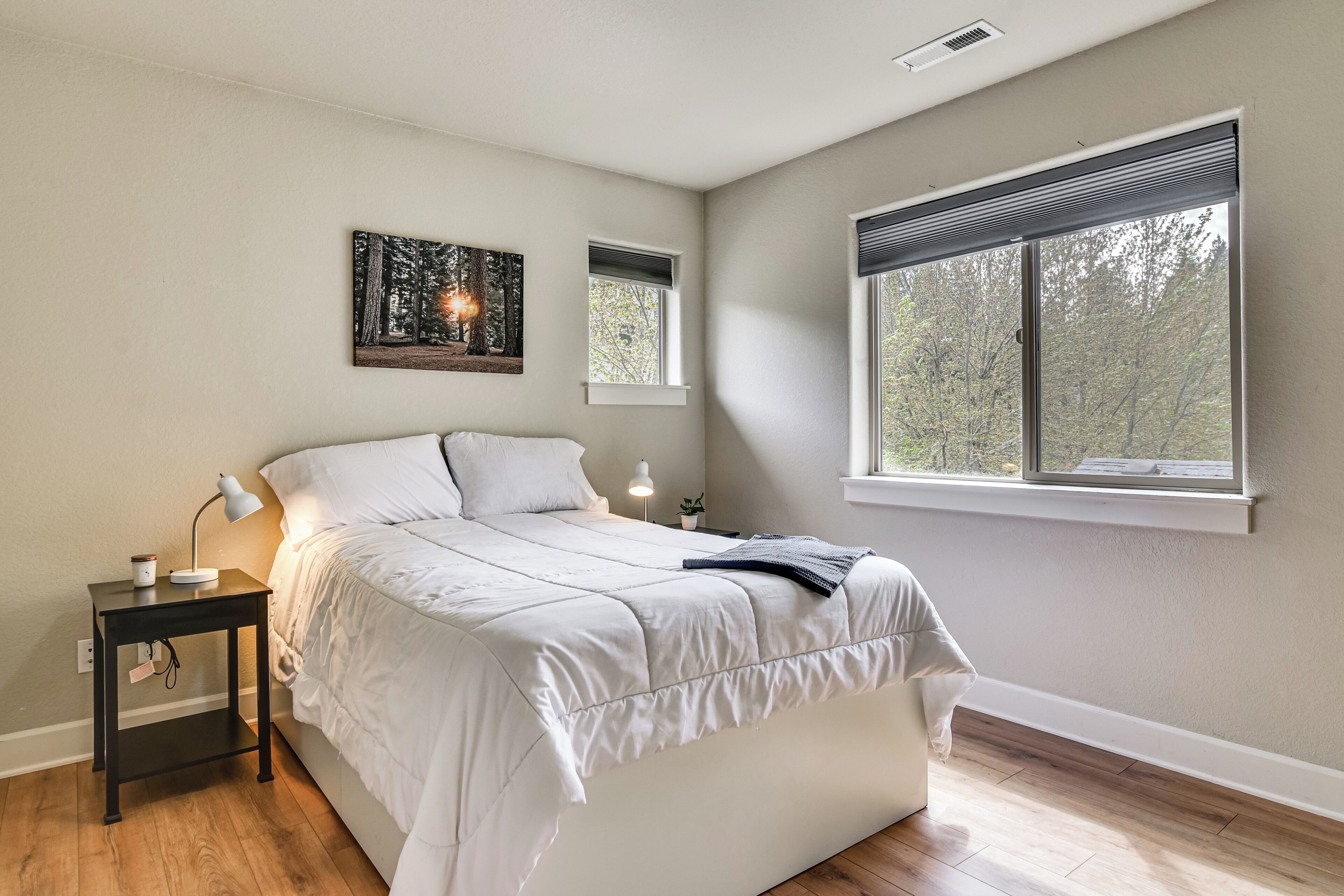 Un dormitorio con cama, mesita de noche, lámpara y ventana con vista a árboles.