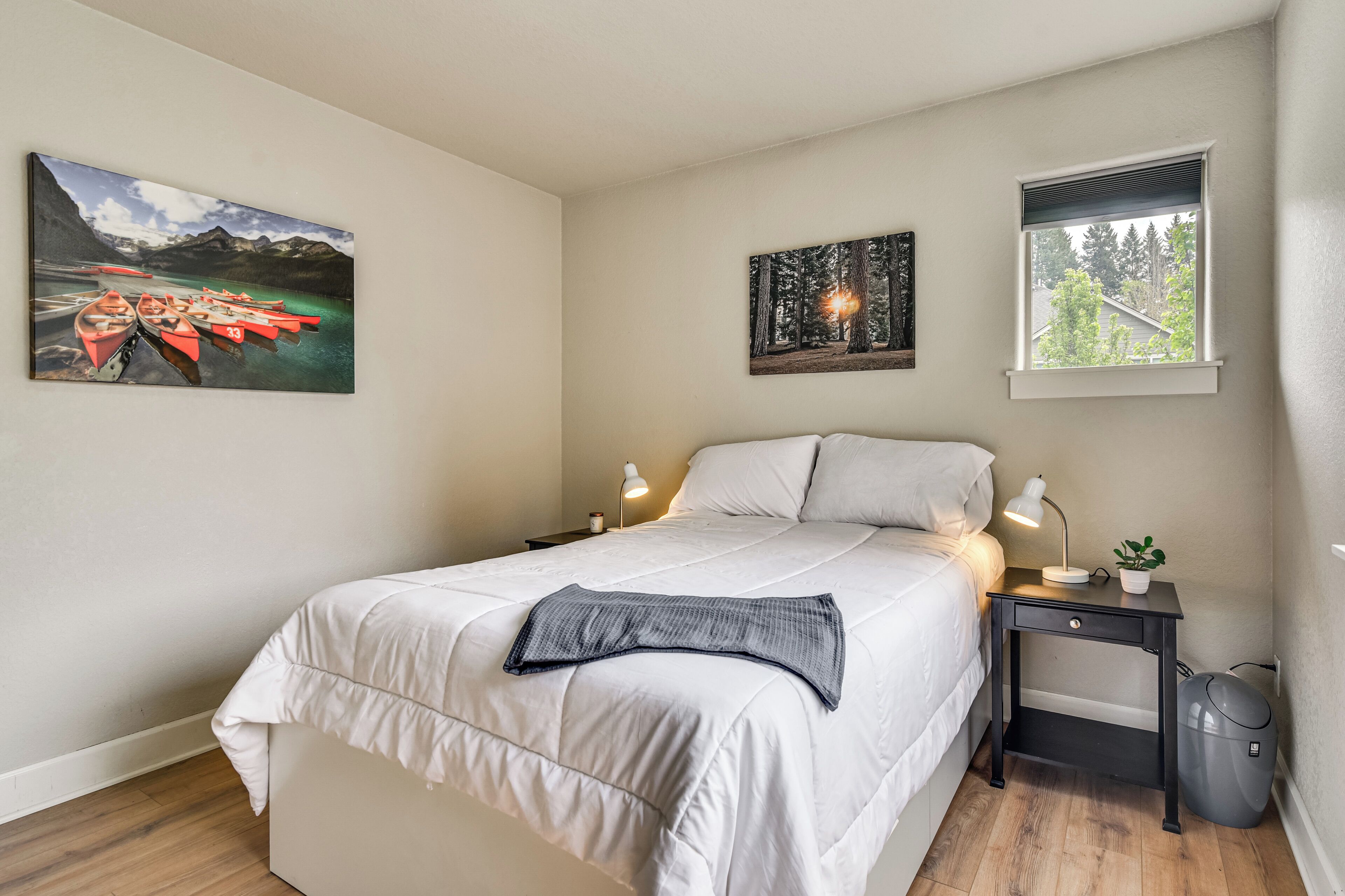 A bedroom with a bed, bedside tables, a lamp, a small plant, and two paintings on the wall.