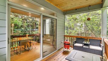A covered deck with a sliding glass door, a grill, outdoor furniture, and a view of a garden.
