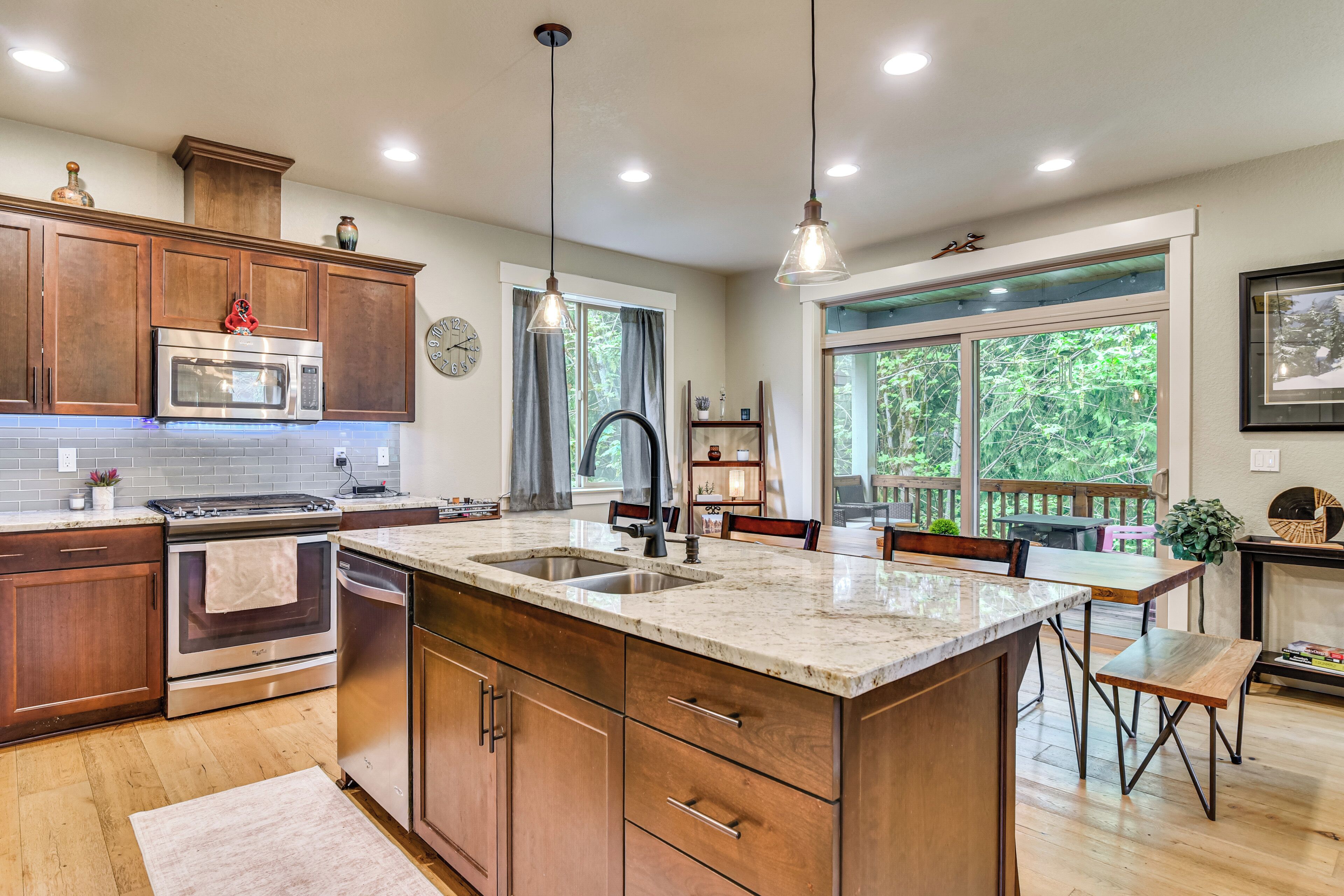 A kitchen with wooden cabinets, stainless steel appliances, a large island with a sink, pendant lighting, and a view of the outdoors through large windows.