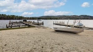 Ein Steg am See mit einem Boot namens 'GRUMMAN' und einem kleinen Gebäude, umgeben von bewaldetem Gelände.