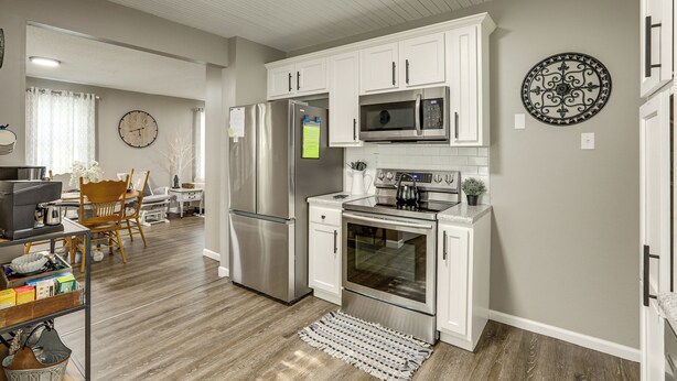 A modern kitchen with white cabinetry, stainless steel appliances, and a dining area with wooden chairs. - Missouri Wine Country Retreat w/ Hot Tub & BBQ (Imperial)