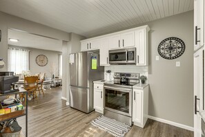 A modern kitchen with white cabinetry, stainless steel appliances, and a dining area with wooden chairs.