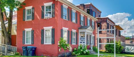 A red brick building with white trim and shutters, a small porch, and a well-maintained lawn.