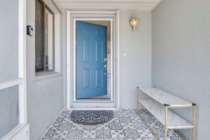 A blue door with a white frame, a small bench, a patterned floor, and a wall-mounted light fixture. - Palm Bay Home w/ Fenced Yard: 10 Mi to Beach! (Palm Bay)