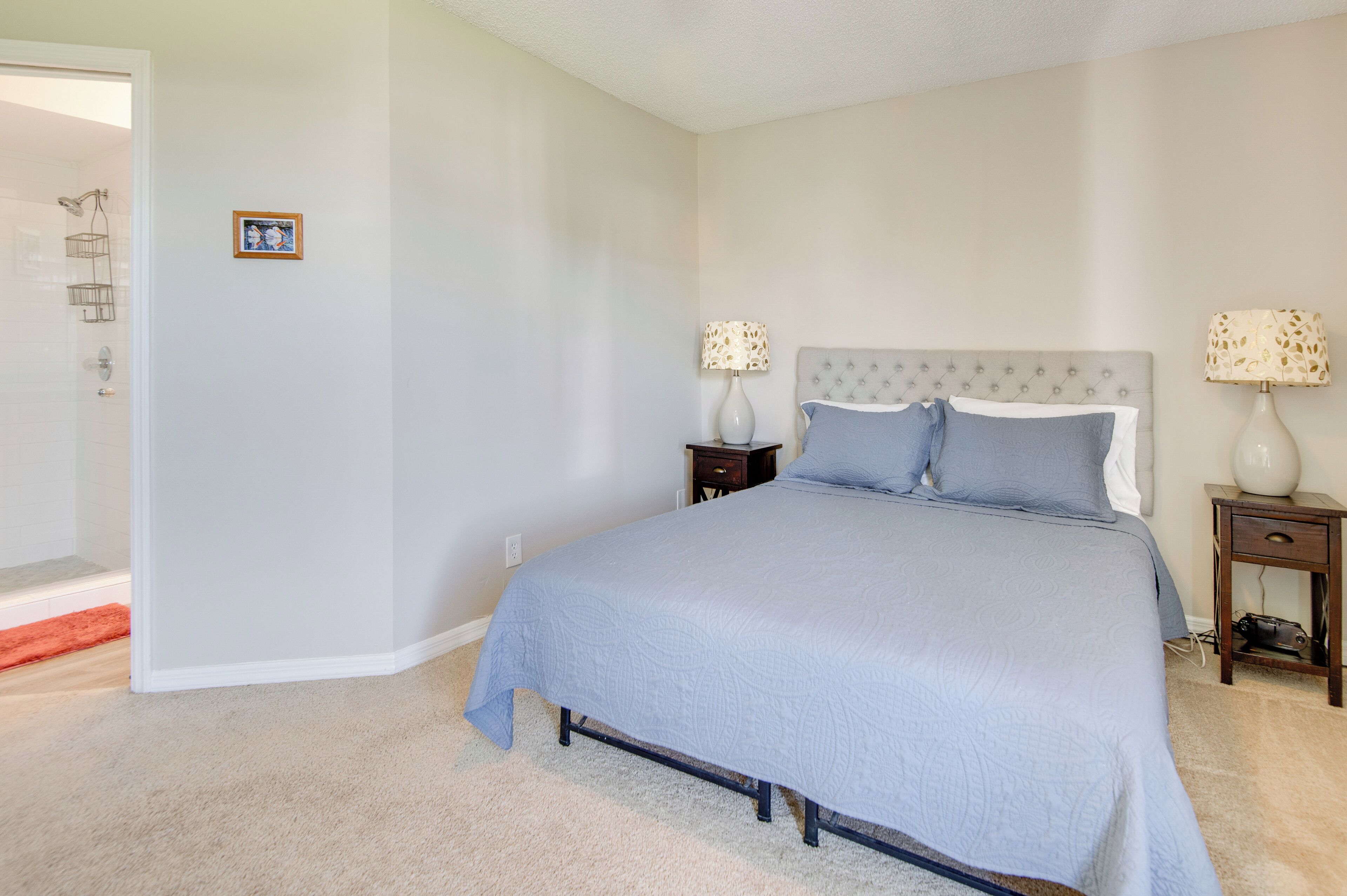 Une chambre à coucher avec un lit, deux tables de chevet avec des lampes, un tableau au mur et un espace douche.
