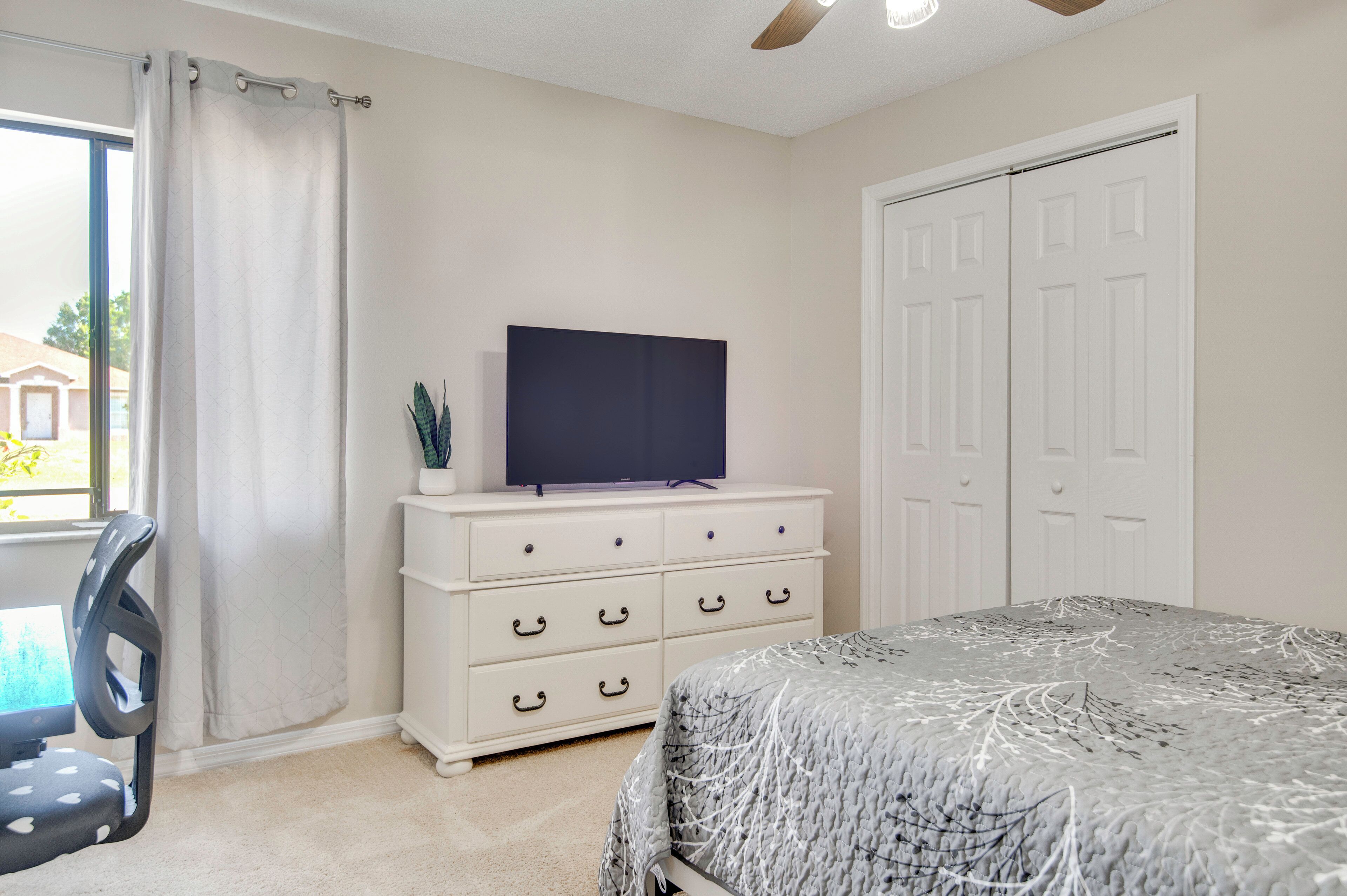 A bedroom with a bed, a TV on a dresser, a chair, and a closet.