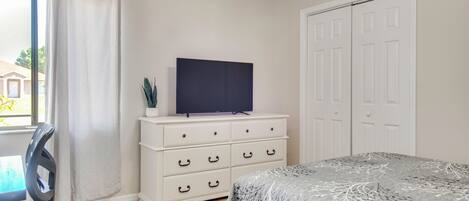 A bedroom with a bed, a TV on a dresser, a chair, and a closet.