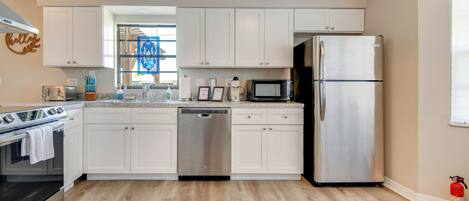 A modern kitchen with white cabinets, stainless steel appliances, and a wooden floor.