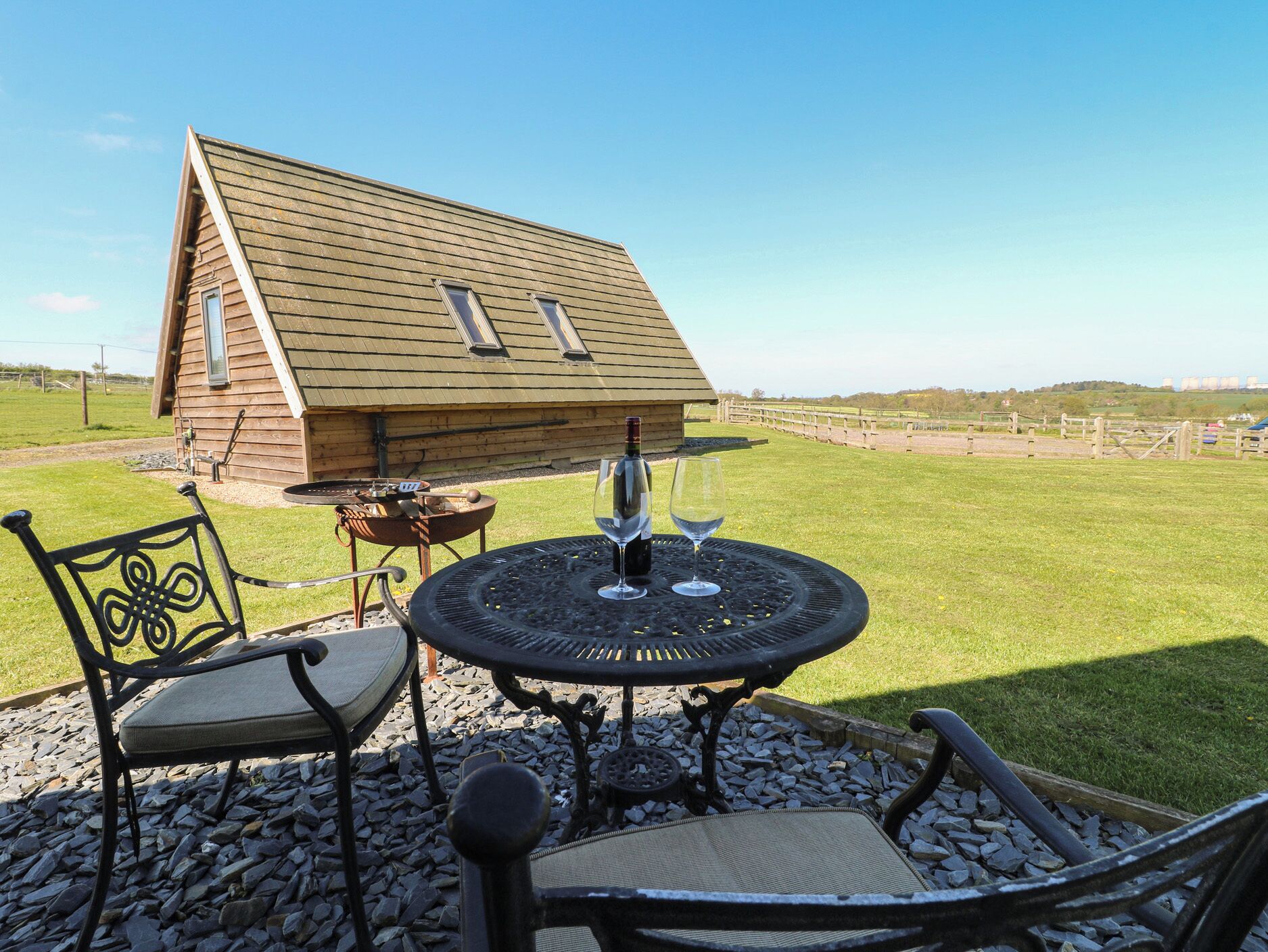 Une cabane en bois avec un toit en pente, une table ronde extérieure avec des chaises, et une vue dégagée sur le paysage environnant.