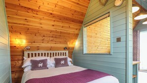 Un dormitorio con techo de madera, una cama con cabecera, una ventana con persianas y una mesita de noche.