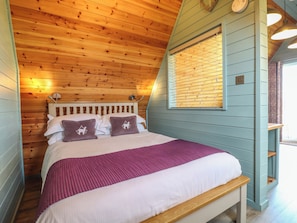 A bedroom with a wooden ceiling, a bed with a headboard, a window with blinds, and a bedside table. - Skylark (Loughborough)