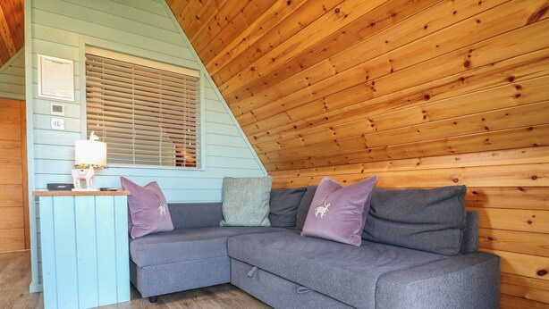 Una habitación acogedora con un sofá seccional gris, una mesita con una lámpara y una ventana con persianas.